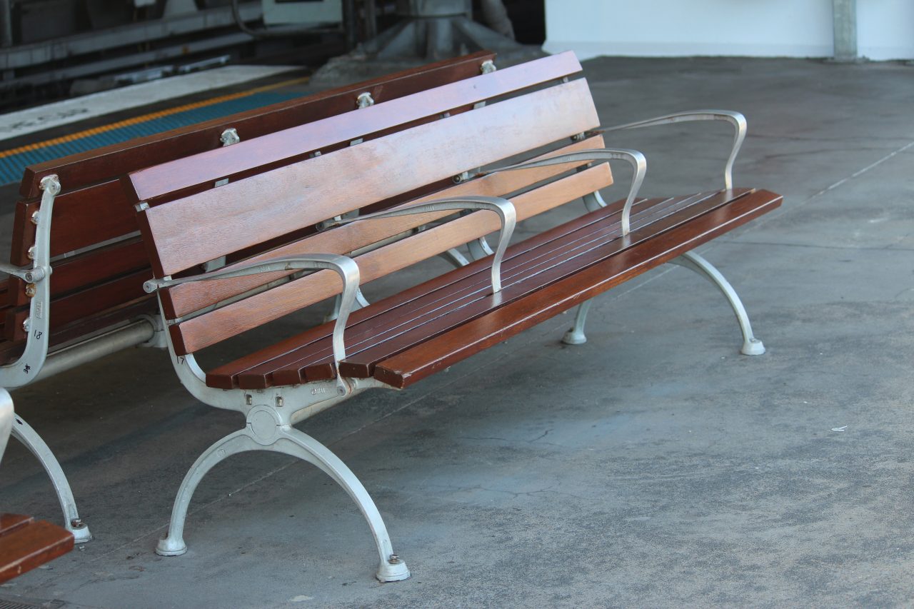 Example of hostile design or aggressive industrial design. A timber and metal bench seat at a train station with four arm rests. The design prevents the homeless from laying down.