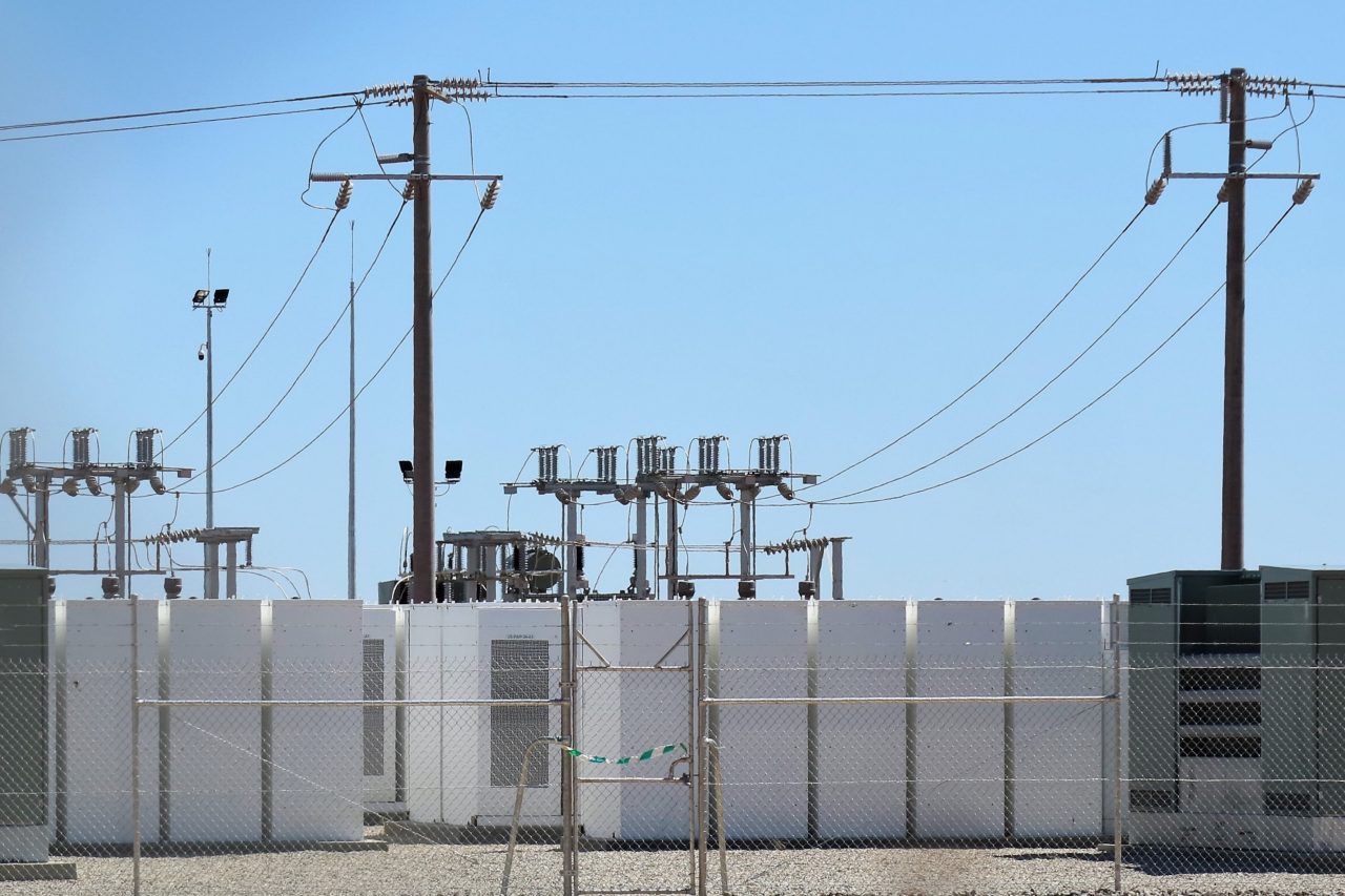 A number of renewable energy batteries stacked behind a wire fence