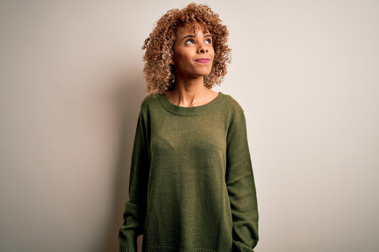 Beautiful african american woman with curly hair wearing casual sweater over white background smiling looking to the side and staring away thinking.