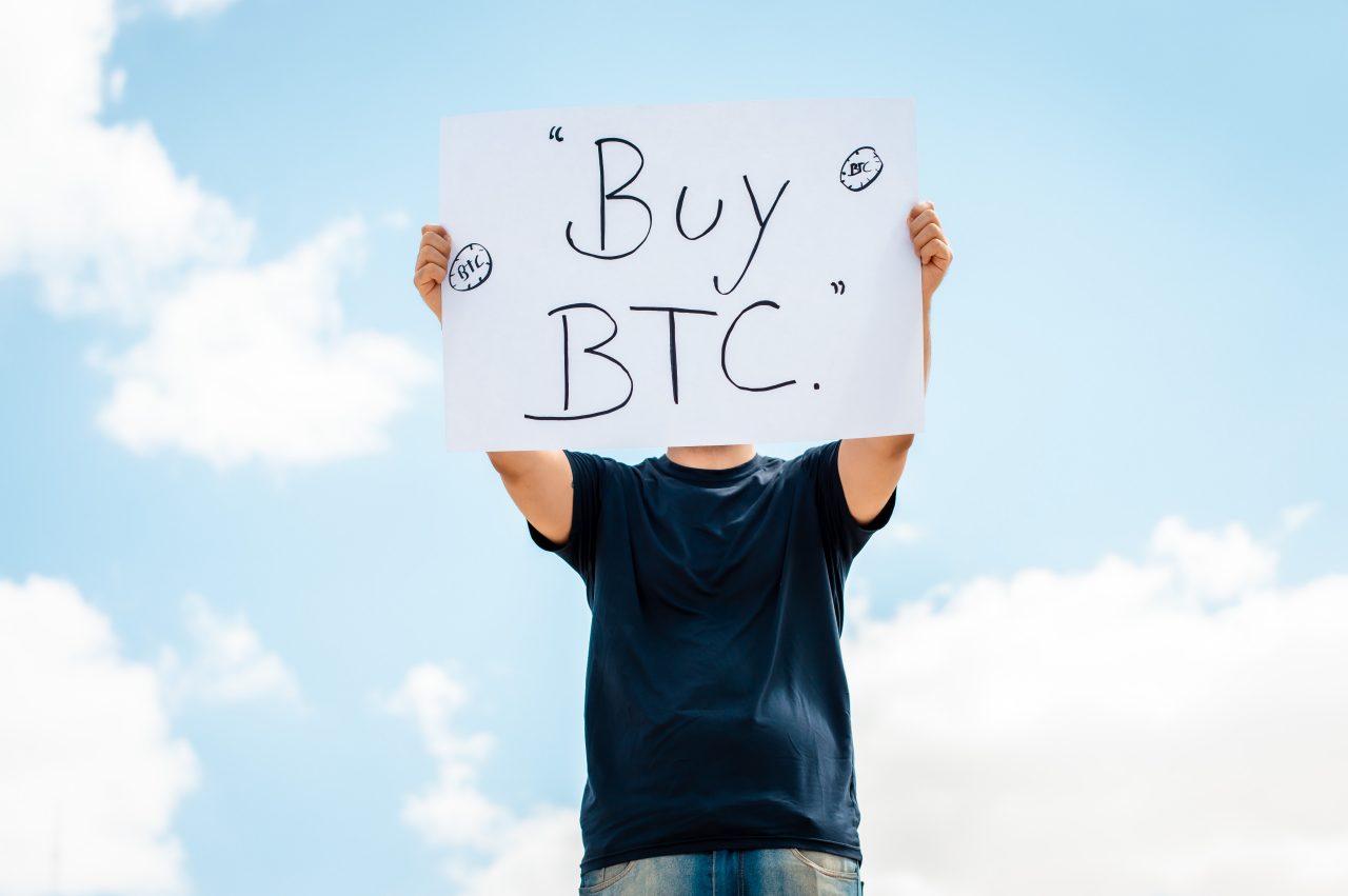 a man holds a sign saying "Buy BTC" meaning, bitcoin