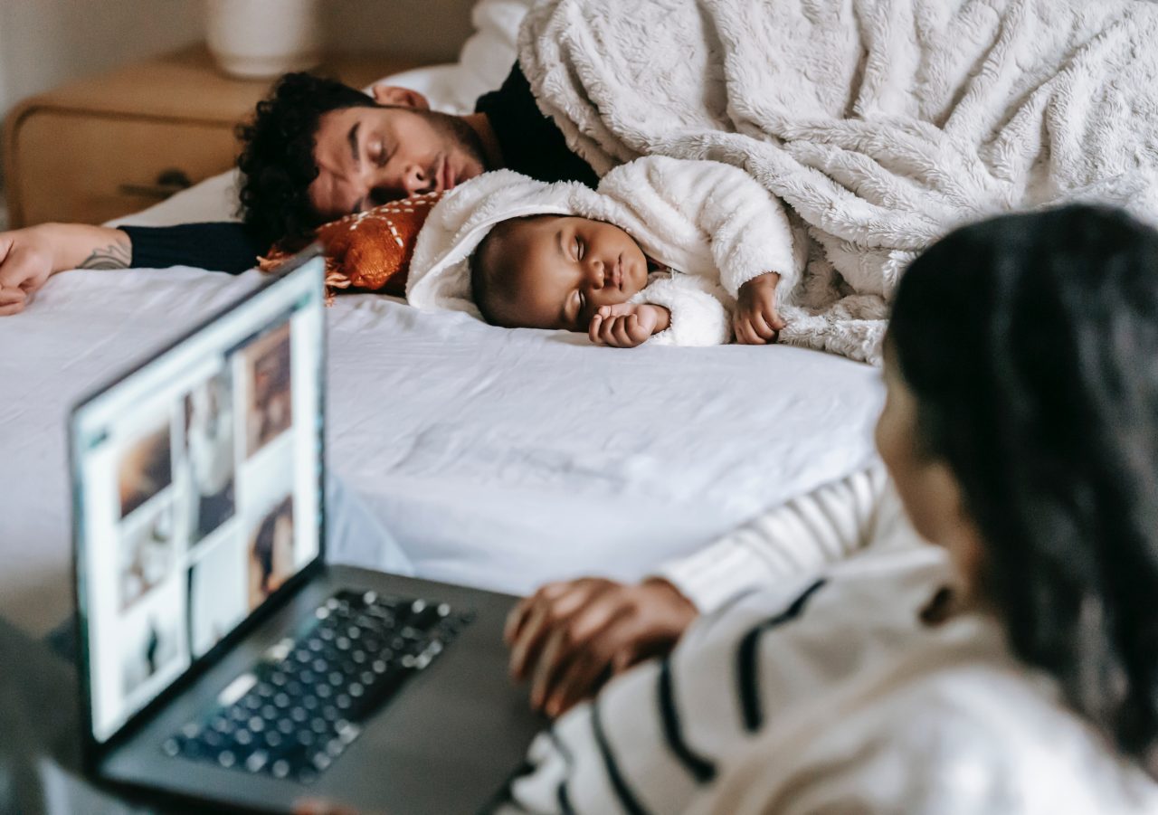 Woman working at laptop looks over at partner and baby sleeping