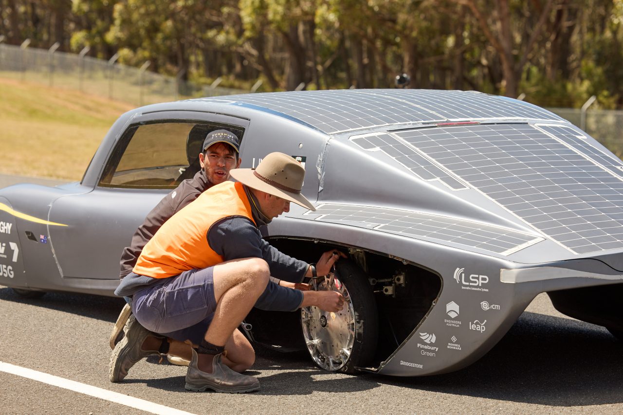 Two members of the Sunswift 7 racing team fixing a rear wheel on the Sunswift 7 car