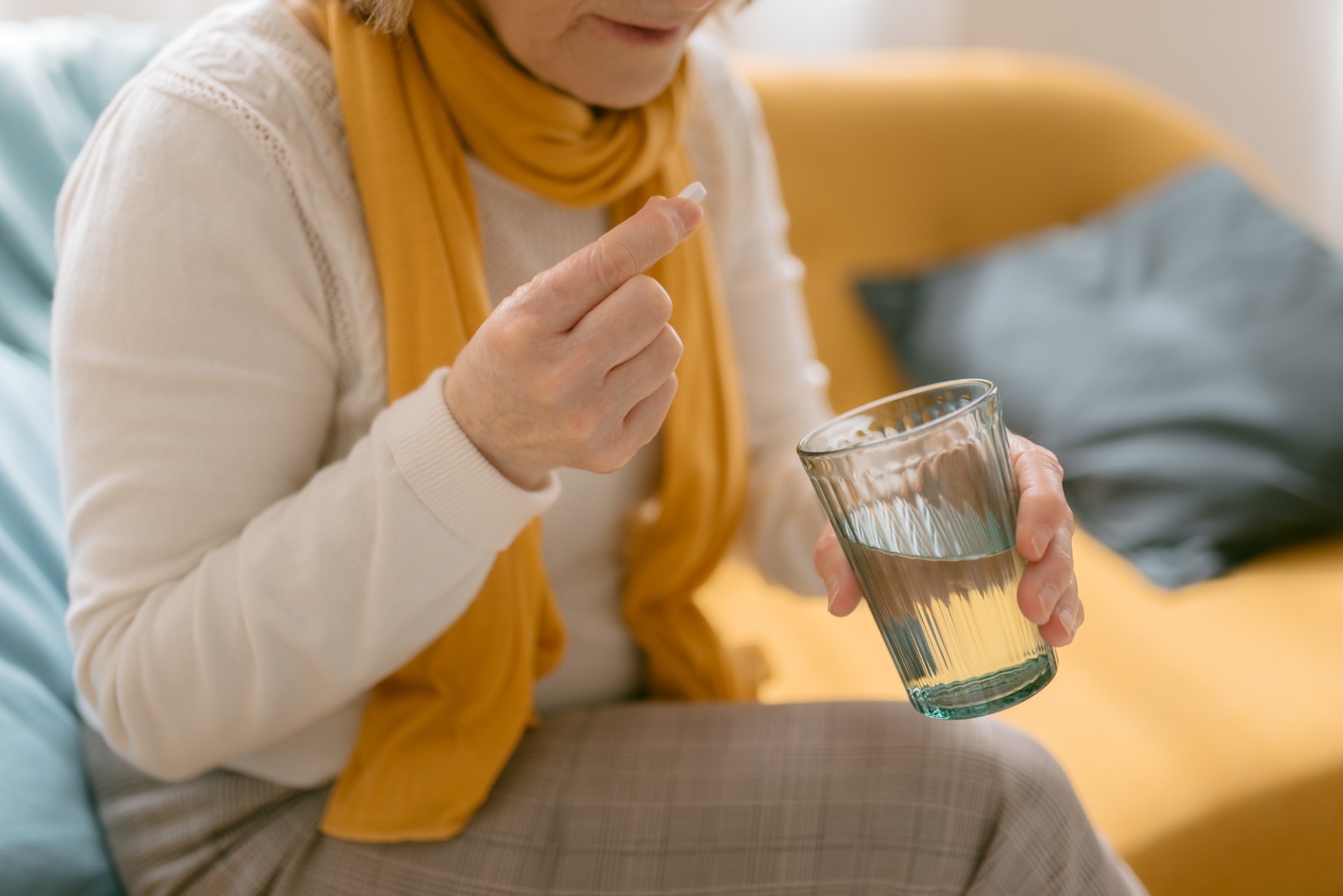 Close up view of mature woman taking a pill. She has a pill in one hand and a glass of water in the other.