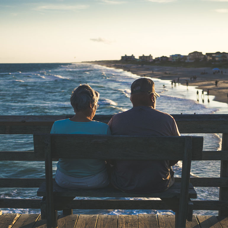 Elderly couple sitting on bench next to ocean