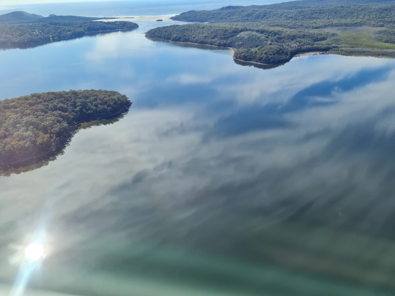 Photo from air of estuarine lake and edge vegetation, clouds reflected in surface of water