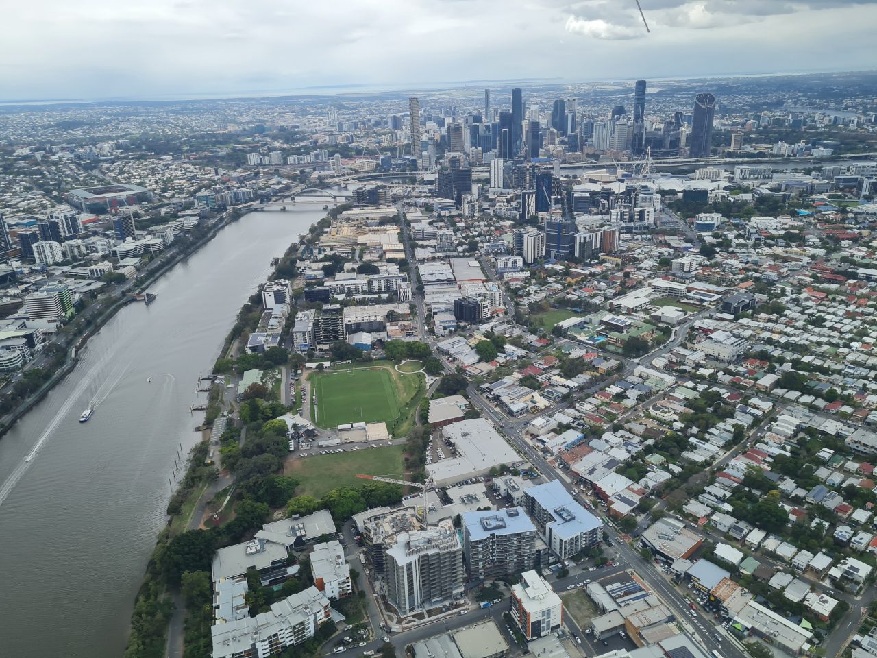 Photo from air of CBD tall buildings and surrounding lower buildings on either side of  river  with boats and bridges