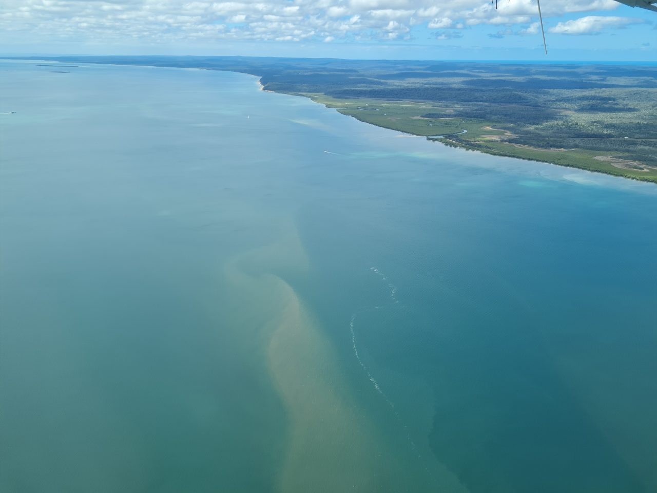 Aerial photo of blue-green ocean water with sand marking current flow surrounding tropical green vegetated island