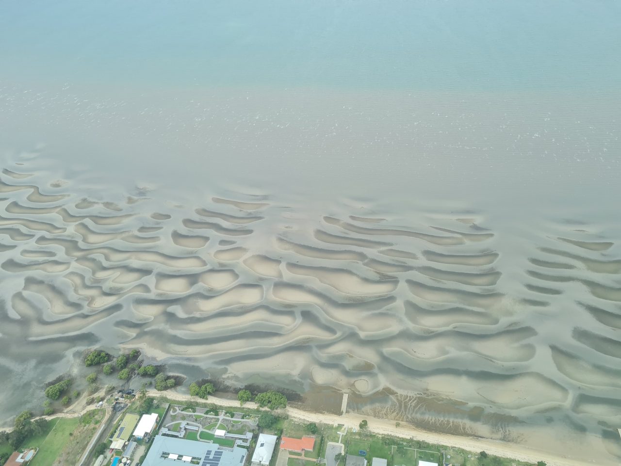 Photo of estuary coastline with intricate sand dune formation surrounding pools of water as tide changes
