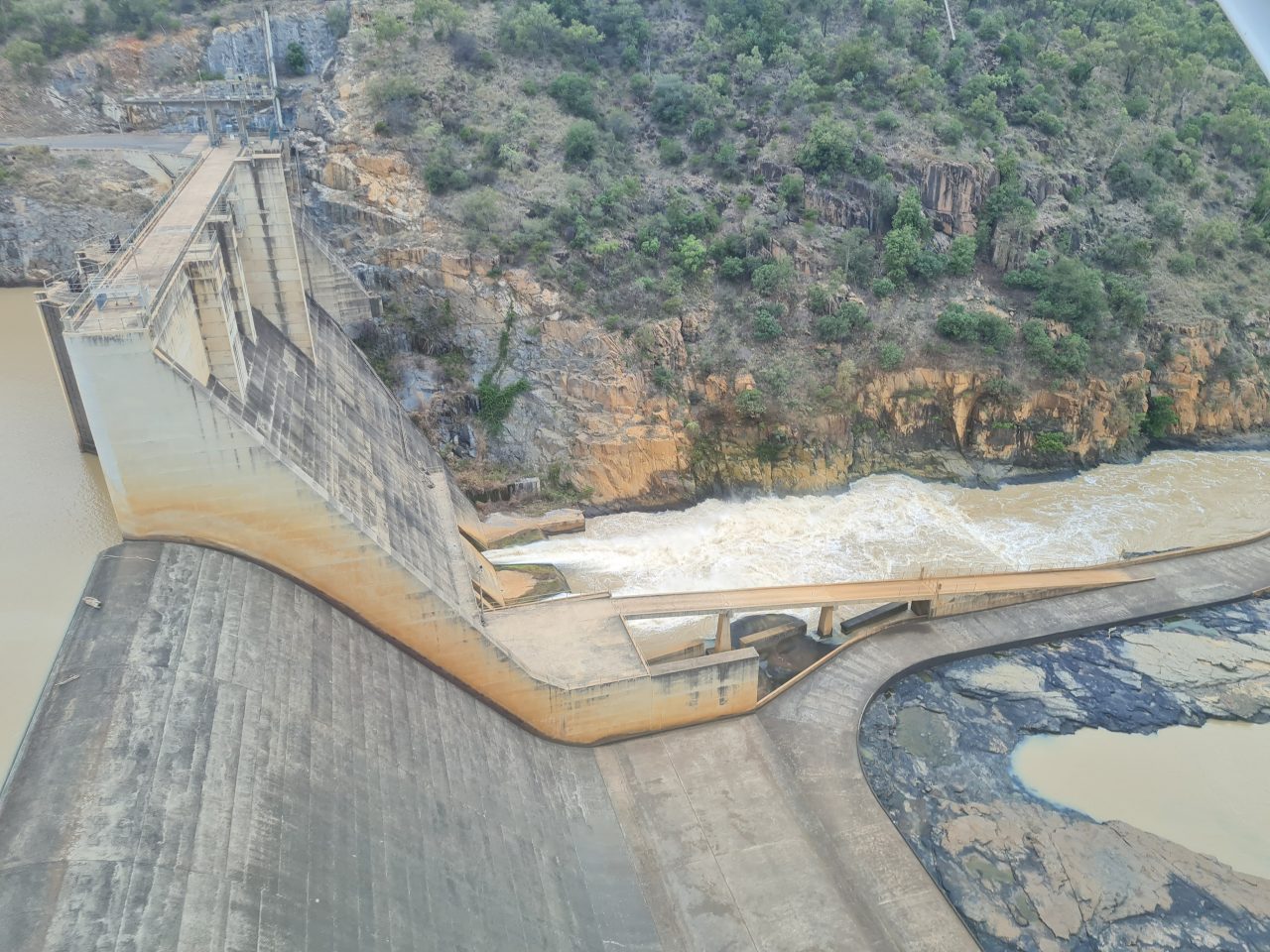Aerial photo of  dam on river, with a flow of yellow-brown water being released