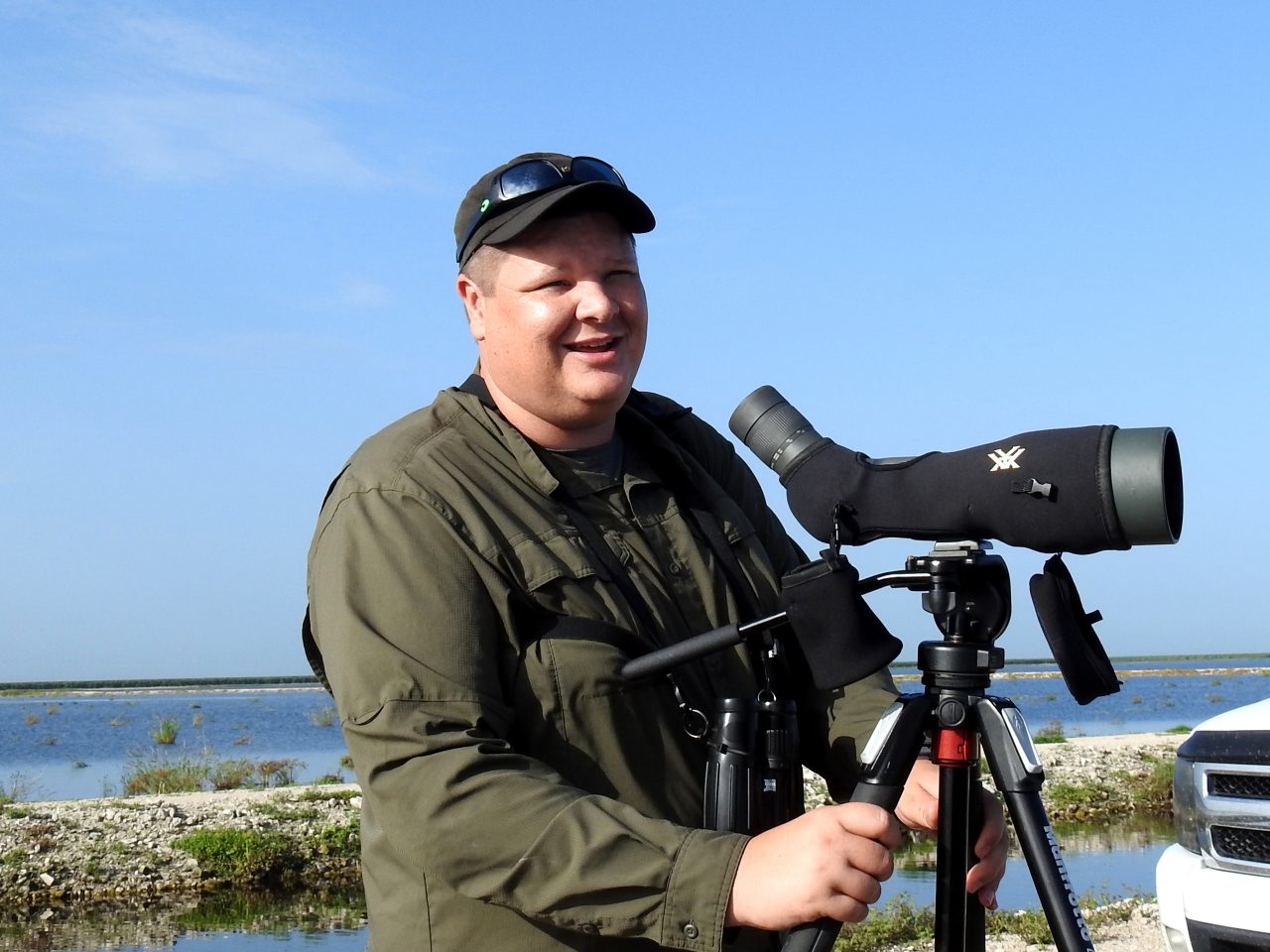 Dr Corey Callaghan with a telescope on a tripod at a wetland