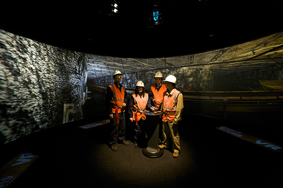 Miners standing in the centre of the AVIE 3D visualisation system, looking at a VR projection of an underground mine.