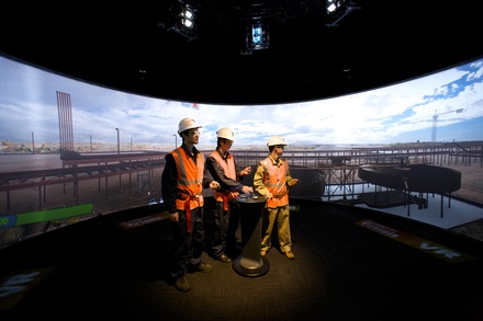 Construction workers stand in front of a projection of a work site.