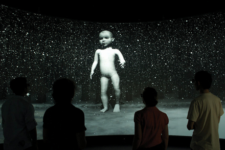 People viewing the projection of a large toddler figure.