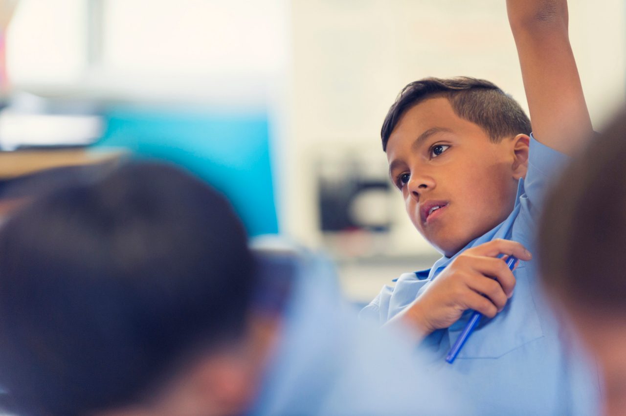Aboriginal Schoolboy with arm raised in classroom. He is wearing a school uniform.