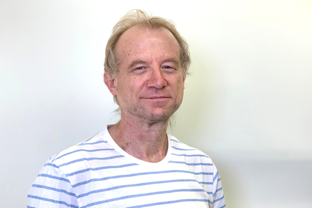 Dr. Philip Van Zanden in a white and blue striped T-shirt, posing with a calm expression against a light wall.