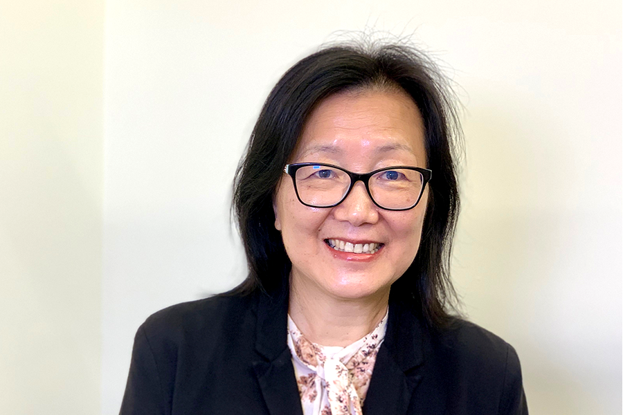 Dr. Yu Zhang in a black blazer, floral blouse, and glasses, smiling warmly against a light background.