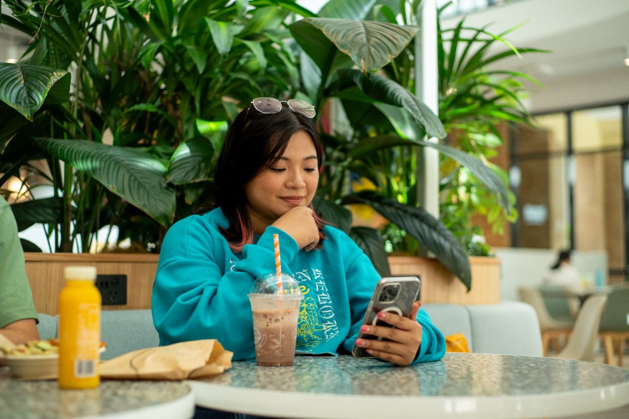 A student looking at their phone while eating food infdoors on Kensington Campus