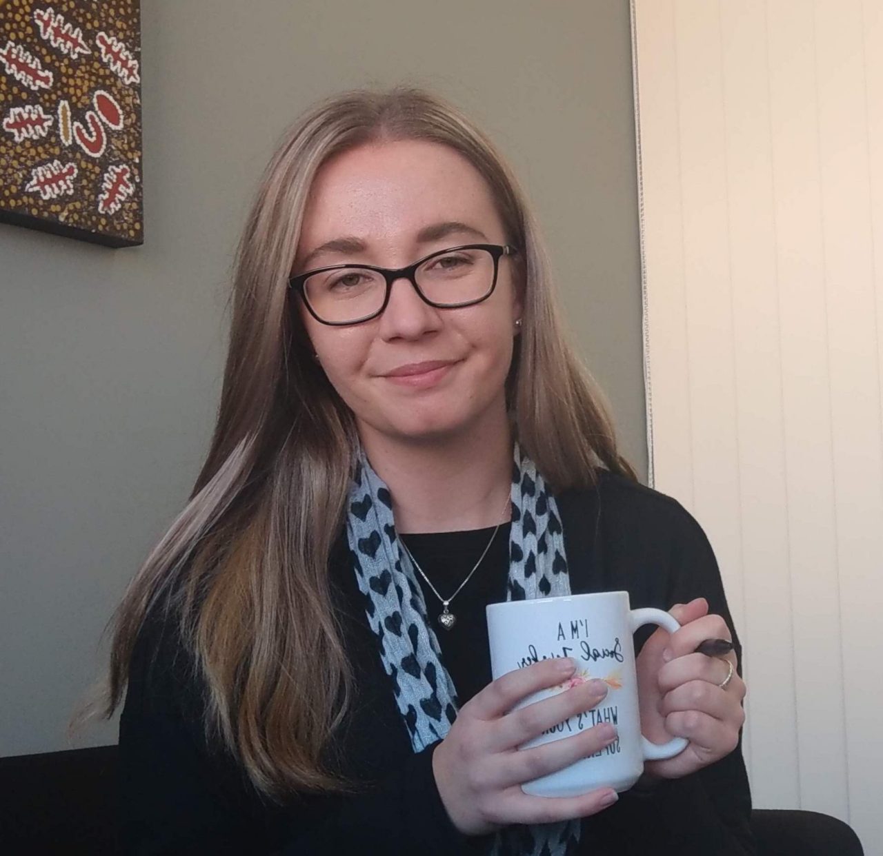 Emily Olley sits in an office holding a coffee mug.